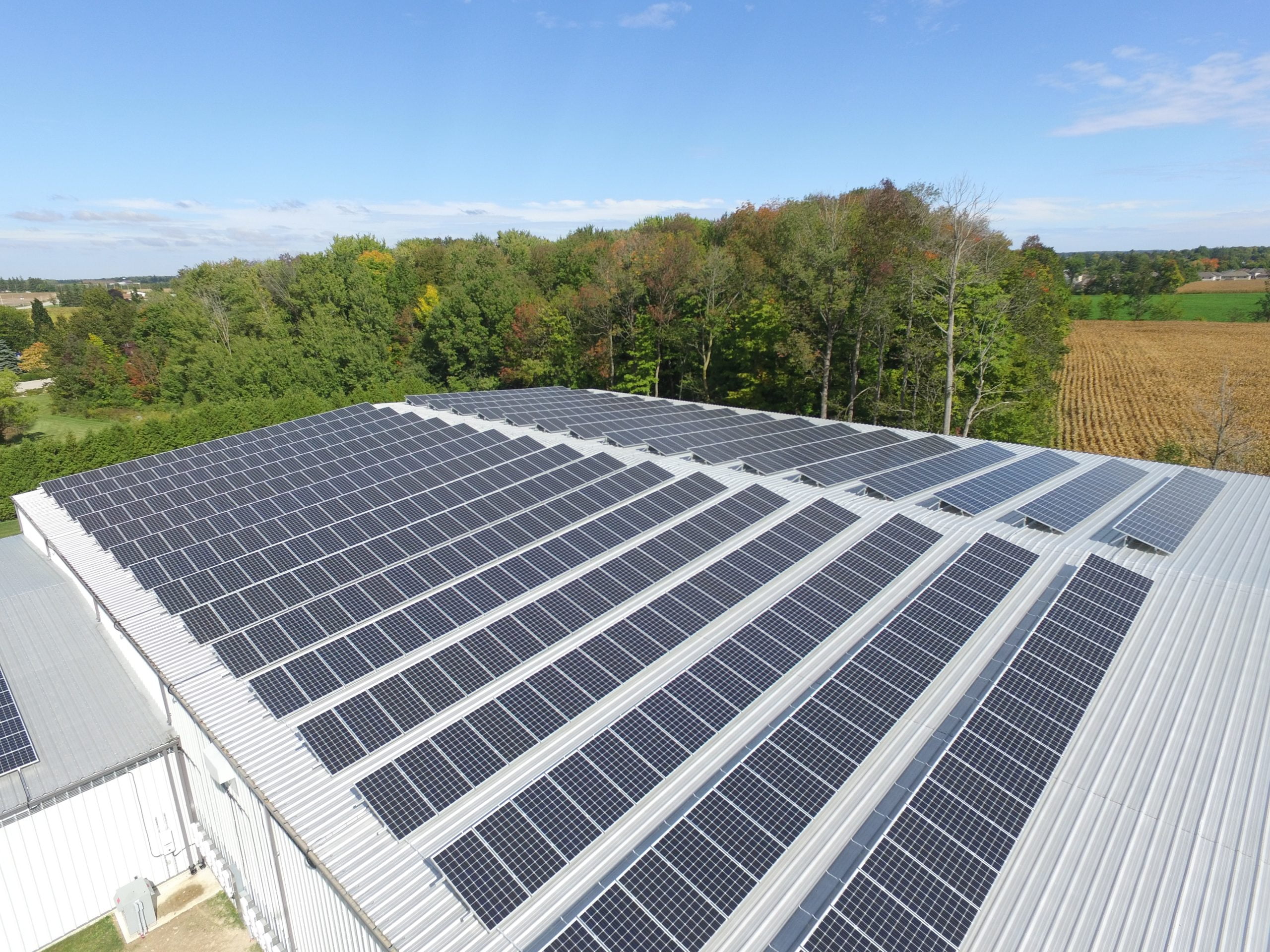 Aerial photo of a solar panel array on the roof of an industrial building in the countryside.