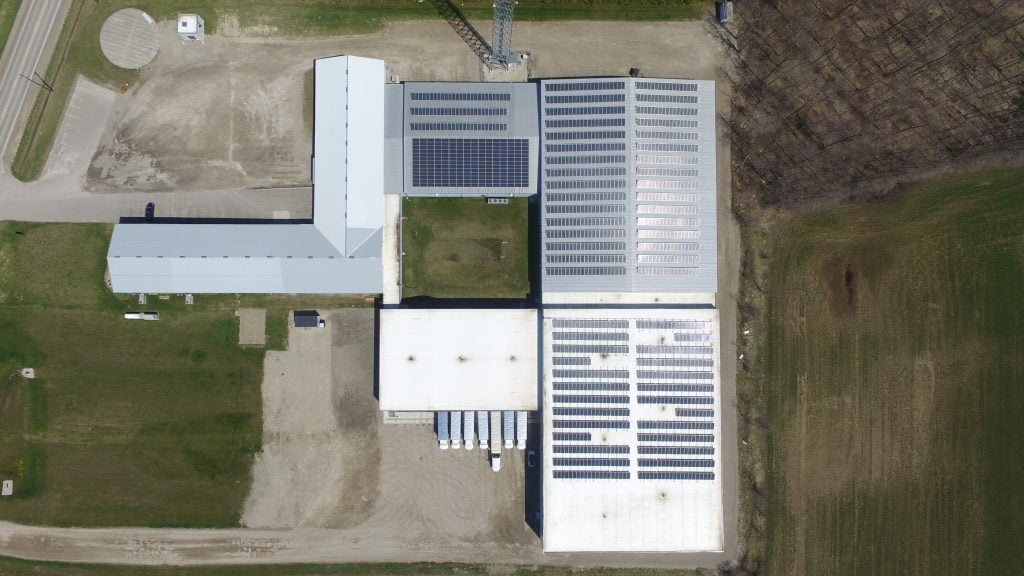 Top down aerial drone photo of hundreds of solar panels on the rooves of a transport depot.