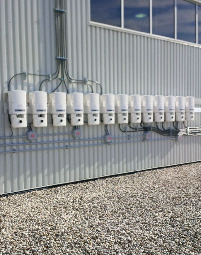 A row of solar panel electrical inverters on the side of a factory wall.